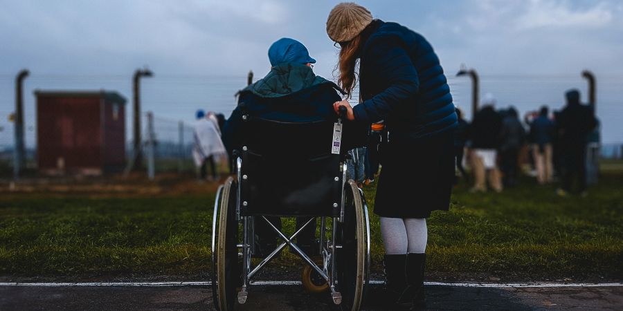 person staning next to someone in a wheelchair, outdoors
