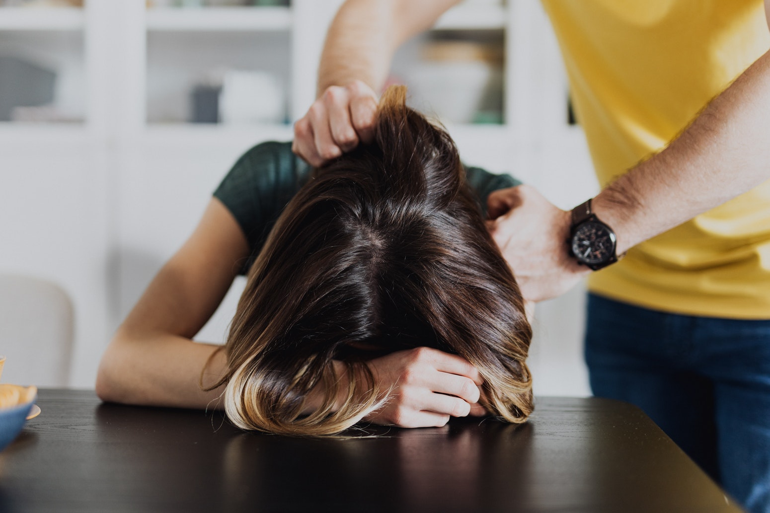 woman's head pressed down on table by a man indoors