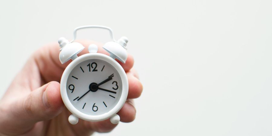 mini white analog clock being held, indoors