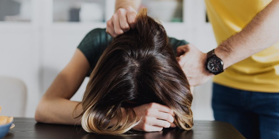 woman's head pressed down on table by a man indoors