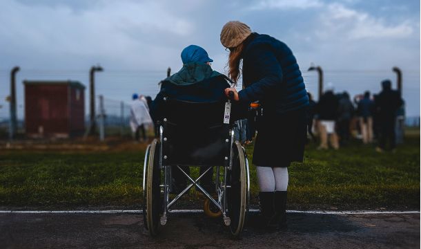 person staning next to someone in a wheelchair, outdoors