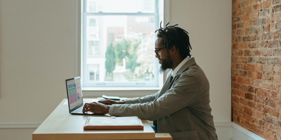 Man typing on a laptop indoors by a window