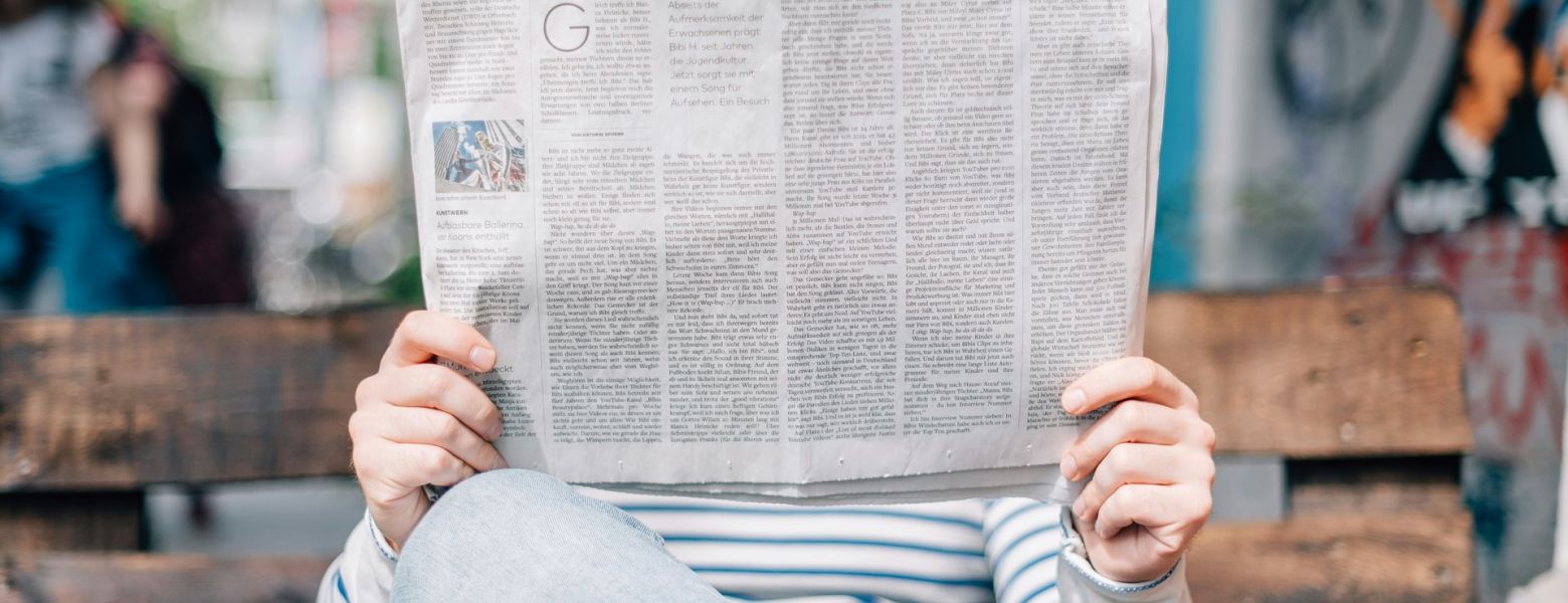 person reading newspaper on bench outside