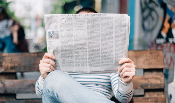 person reading newspaper on bench outside