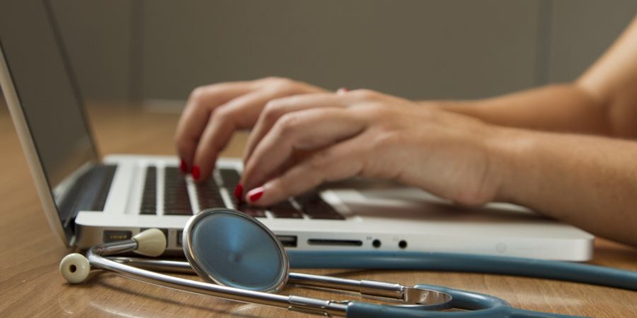 woman using a laptop next to a stethescope indoors on a table