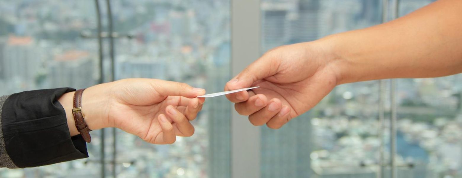 person handing a card to another, indoors with a window in the background