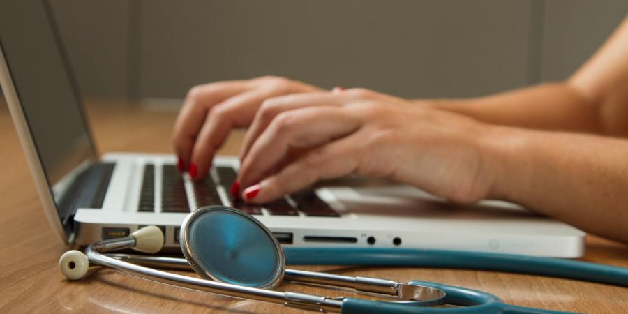 medical person using a laptop indoors at a desk, stethoscope