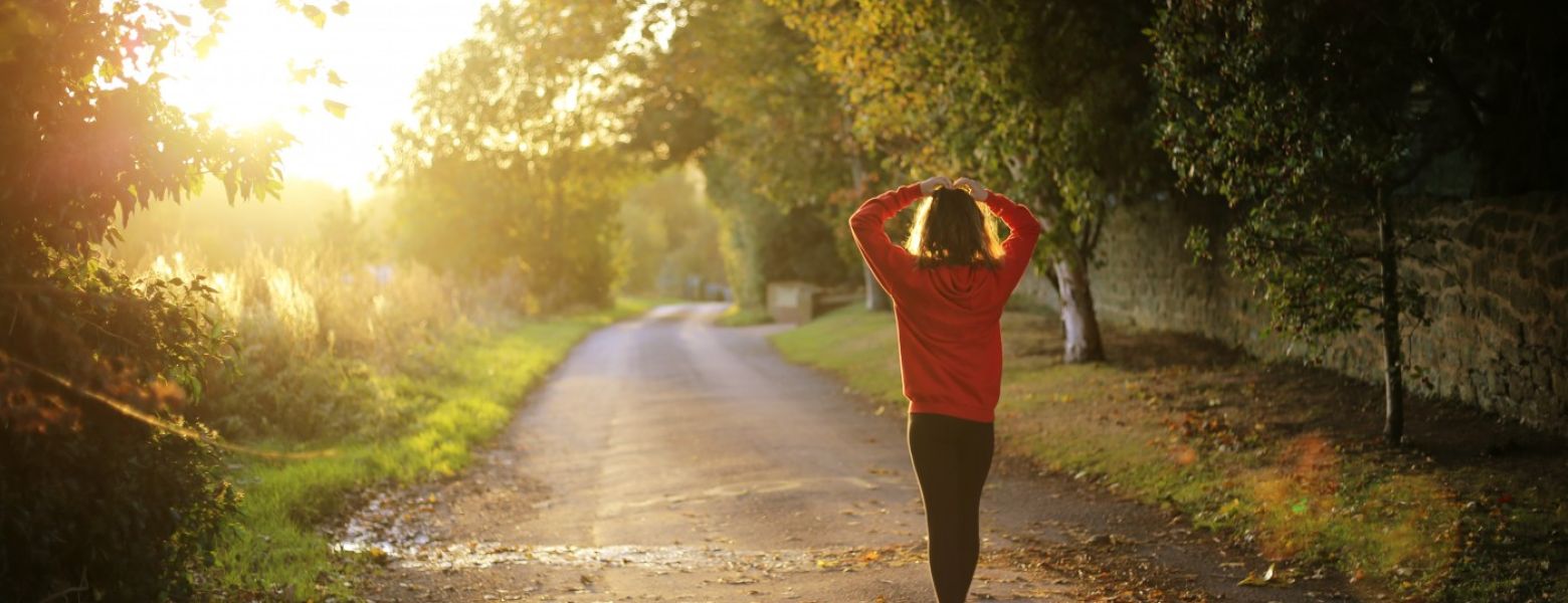 person walking on a road in the sunlight around trees