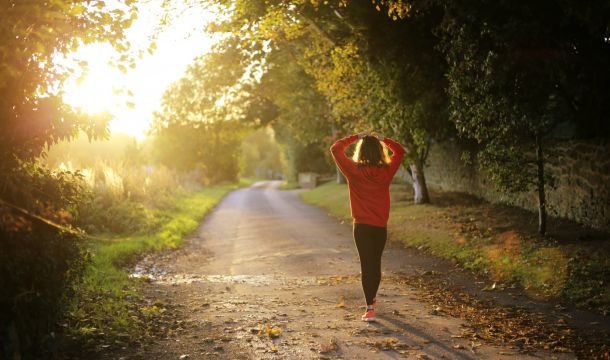 person walking on a road in the sunlight around trees