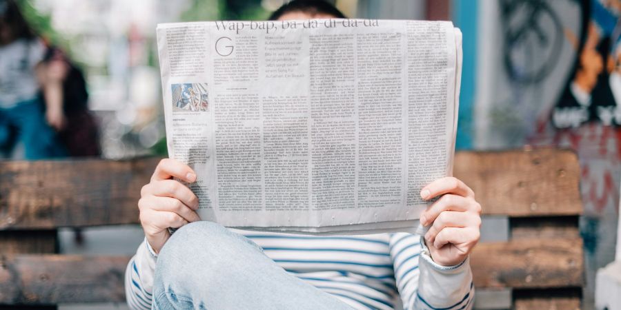 person reading newspaper on bench outside
