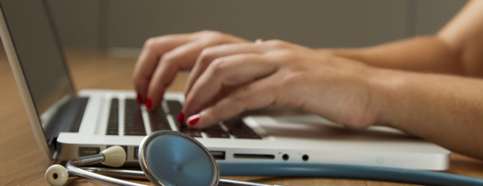 woman using a laptop next to a stethescope indoors on a table