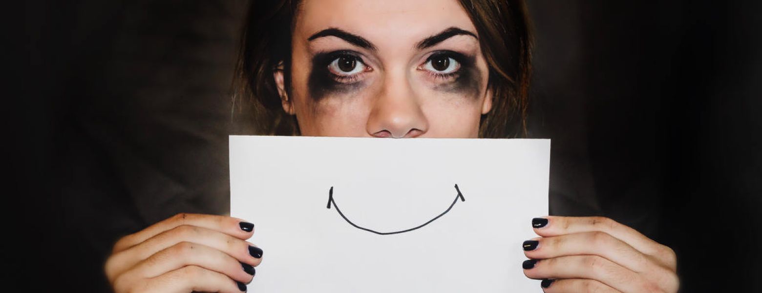 hurt woman hiding behind a smiling sign