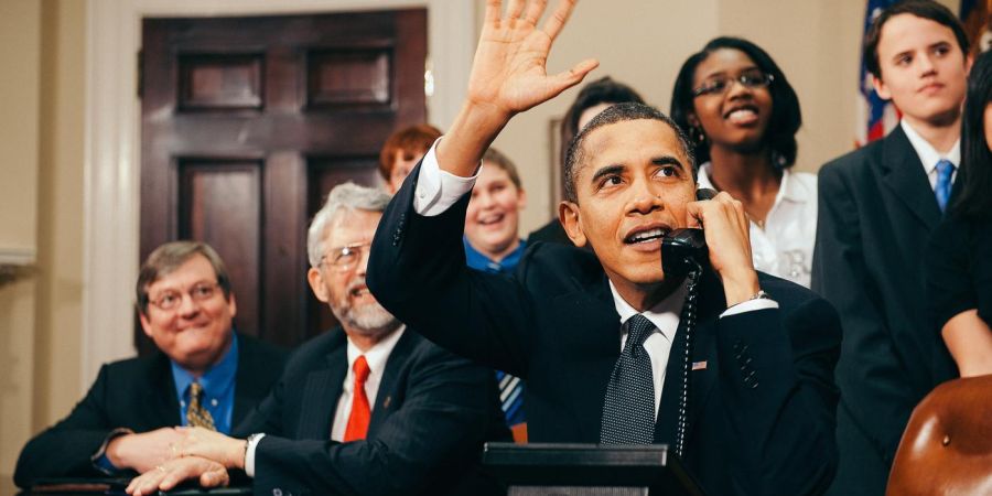 U.S. President Barack Obama, accompanied by members of Congress and middle school children, waves as he talks on the phone from the Roosevelt Room of the White House to astronauts on the International Space Station.