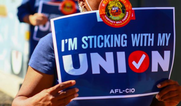 person outdoors standing with a sign that says, I'm sticking with my union