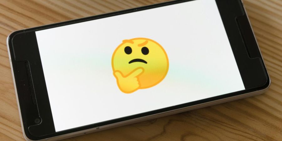 wondering emoji on phone, on wood table, indoors