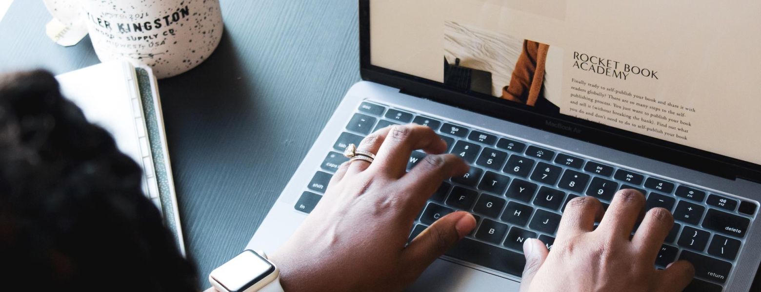 woman typing on a laptop on a table next to a cup of coffee indoors