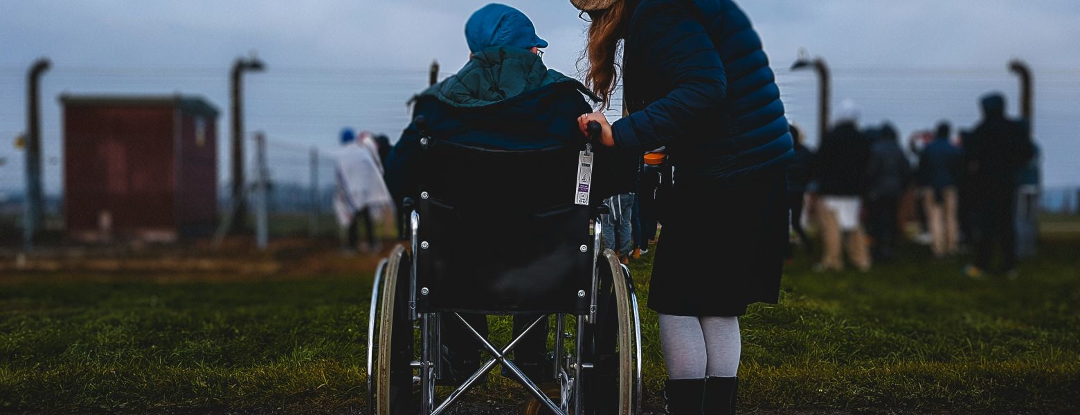 person staning next to someone in a wheelchair, outdoors