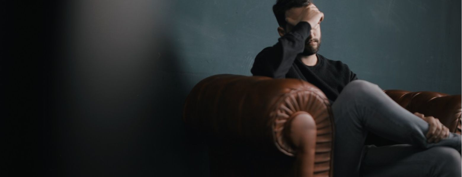 man on couch indoors, hand on his head