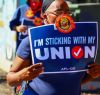 person outdoors standing with a sign that says, I'm sticking with my union