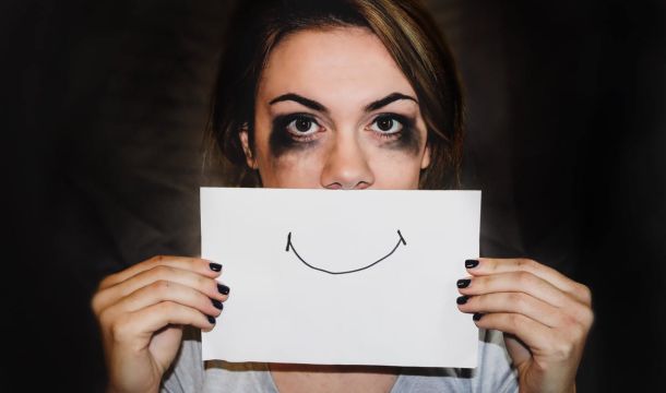hurt woman hiding behind a smiling sign