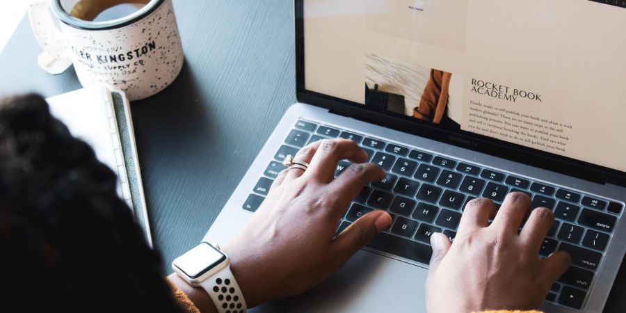 woman typing on a laptop on a table next to a cup of coffee indoors
