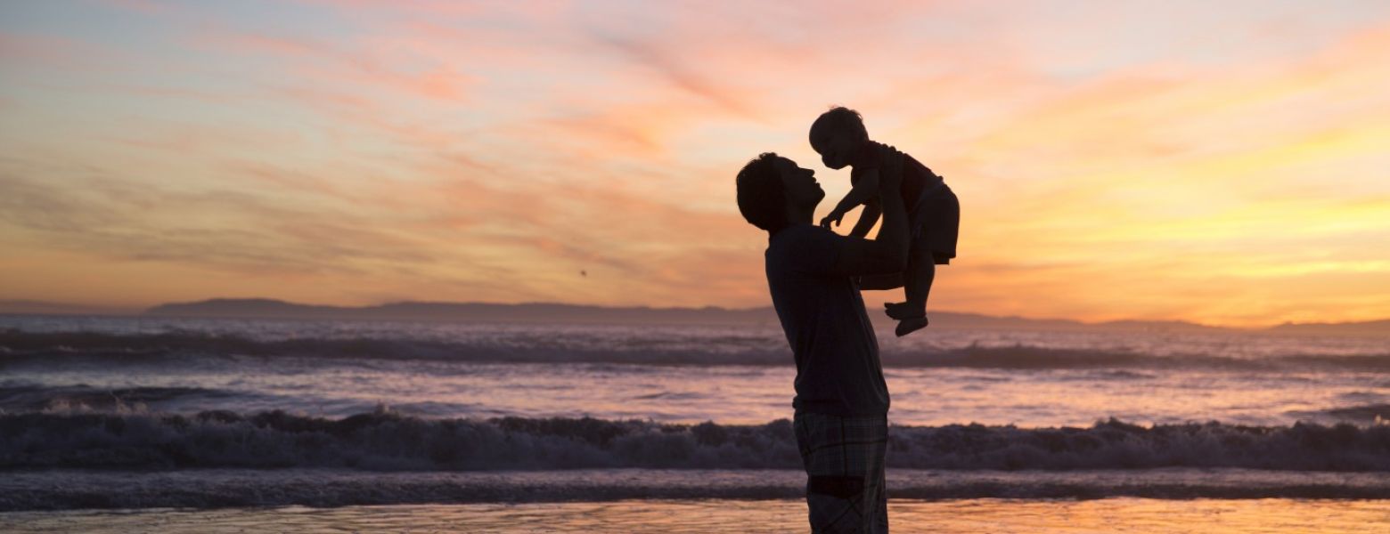 father holding a child up while the sun is setting while standing in the ocean beach