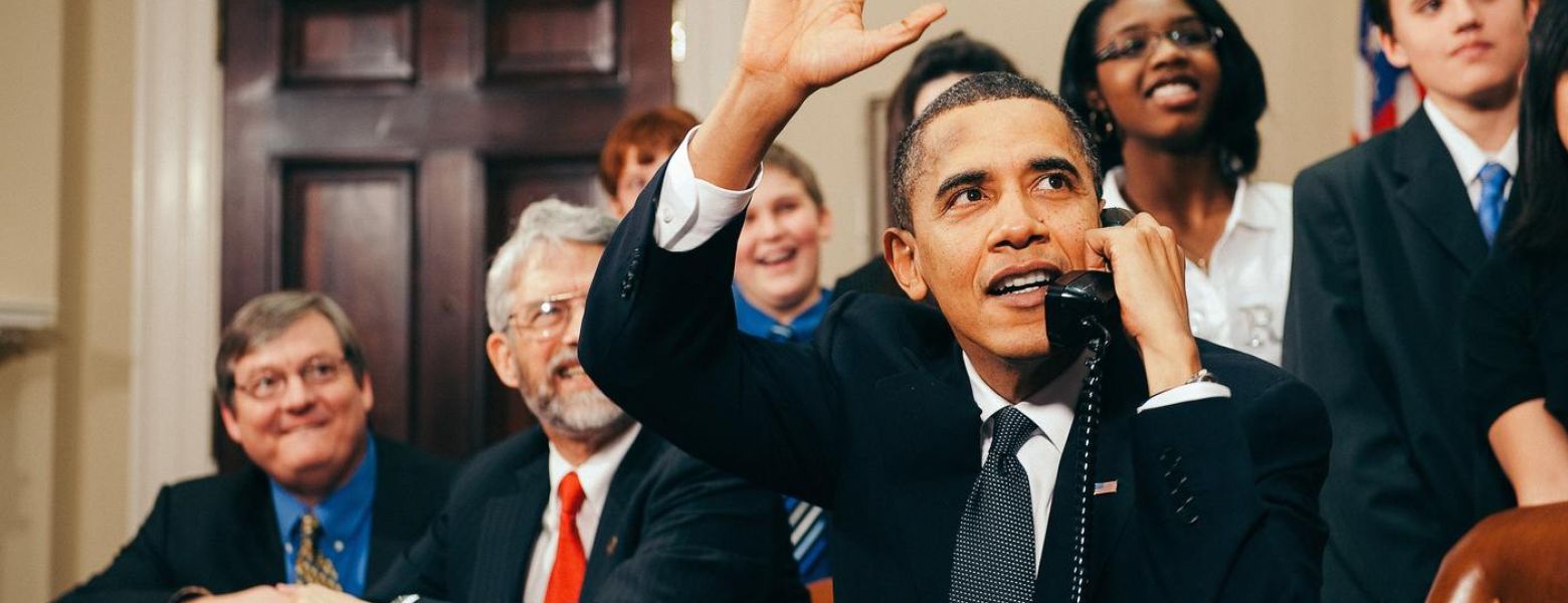 U.S. President Barack Obama, accompanied by members of Congress and middle school children, waves as he talks on the phone from the Roosevelt Room of the White House to astronauts on the International Space Station.