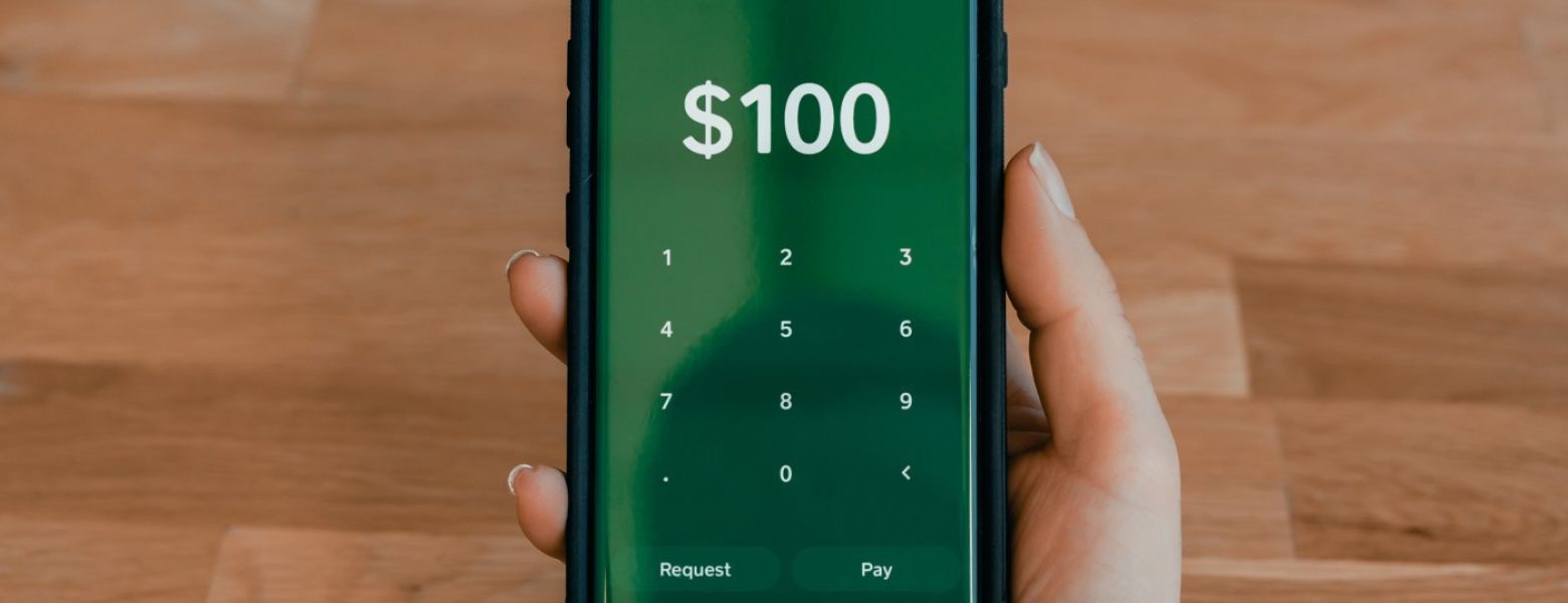 $100 on a clacualator on phone in a hand over a wooden table indoors