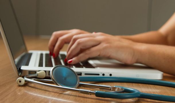 medical person using a laptop indoors at a desk, stethoscope