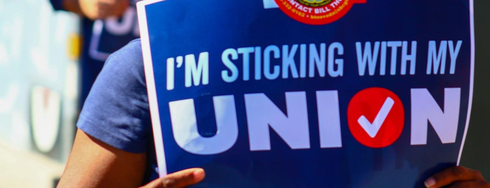 person outdoors standing with a sign that says, I'm sticking with my union