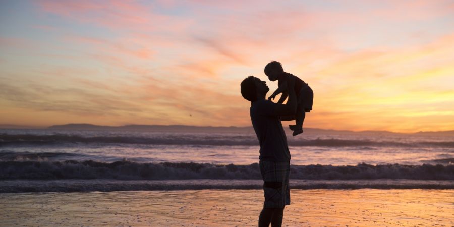 father holding a child up while the sun is setting while standing in the ocean beach