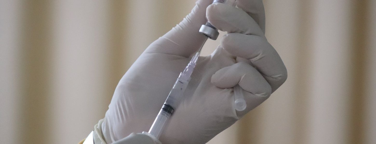 extracting vaccine from vile with needle by gloved person, indoors