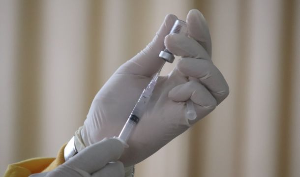 extracting vaccine from vile with needle by gloved person, indoors